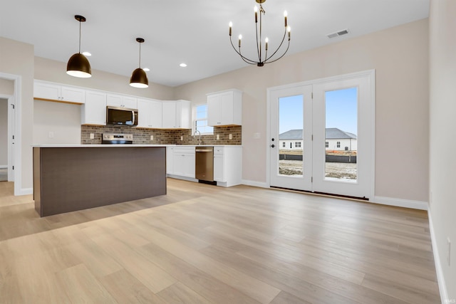 kitchen with appliances with stainless steel finishes, white cabinetry, a center island, decorative backsplash, and decorative light fixtures