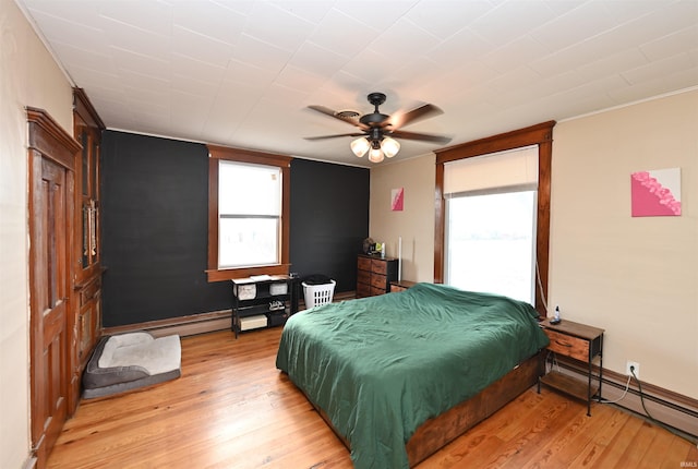 bedroom featuring ceiling fan, a baseboard heating unit, and light hardwood / wood-style floors