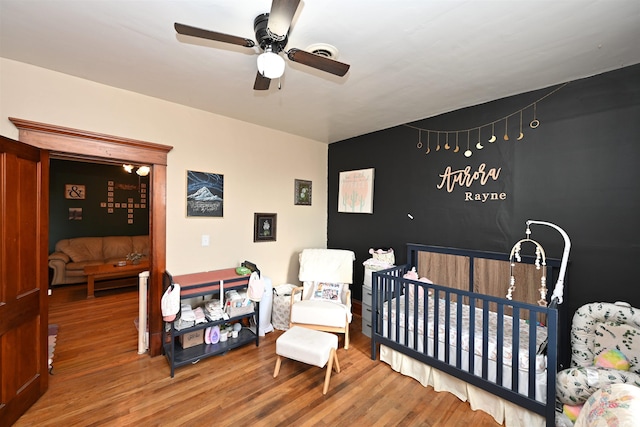 bedroom featuring a crib, wood-type flooring, and ceiling fan