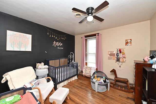 bedroom featuring hardwood / wood-style flooring, ceiling fan, and a nursery area