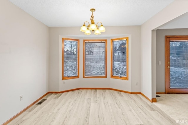 unfurnished dining area featuring an inviting chandelier, light hardwood / wood-style floors, and a textured ceiling