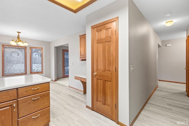 corridor with an inviting chandelier, light hardwood / wood-style floors, and a textured ceiling