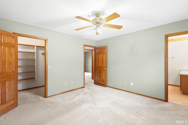 unfurnished bedroom with a spacious closet, light colored carpet, ceiling fan, ensuite bath, and a closet