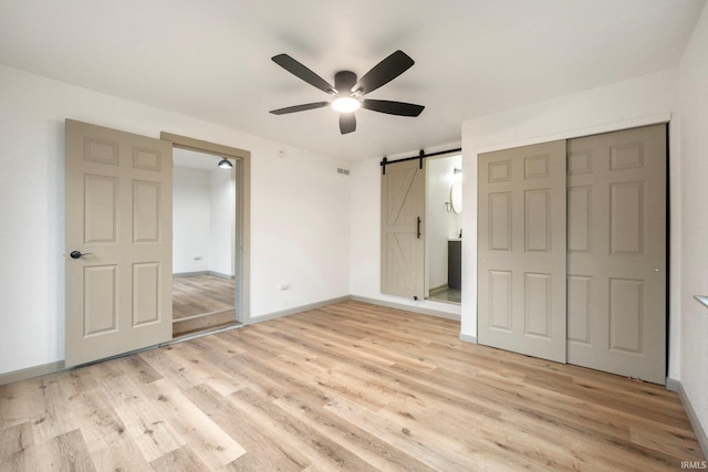 unfurnished bedroom featuring ceiling fan, a barn door, light hardwood / wood-style floors, and a closet