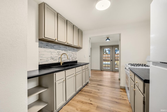 kitchen featuring sink, white appliances, gray cabinetry, light hardwood / wood-style floors, and decorative backsplash