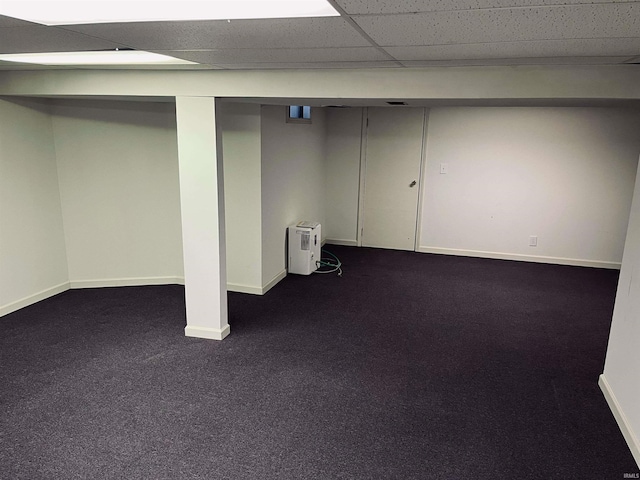 basement with a paneled ceiling and dark colored carpet