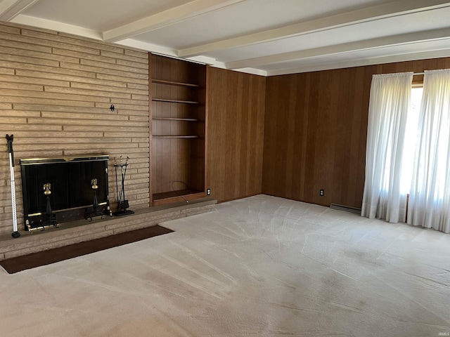 unfurnished living room with a brick fireplace, beam ceiling, light colored carpet, and wood walls