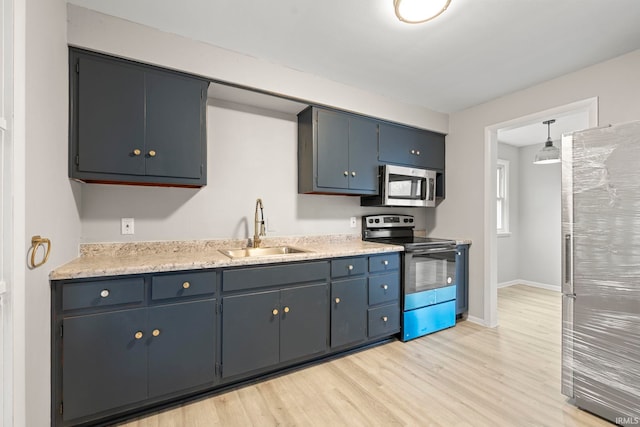 kitchen featuring appliances with stainless steel finishes, pendant lighting, blue cabinets, sink, and light hardwood / wood-style flooring