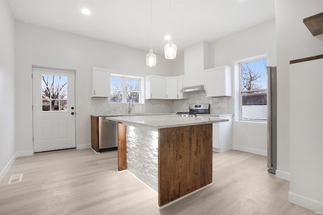 kitchen featuring appliances with stainless steel finishes, hanging light fixtures, a center island, extractor fan, and white cabinets