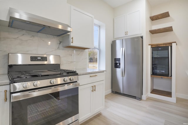 kitchen featuring wall chimney exhaust hood, white cabinetry, light stone counters, stainless steel appliances, and backsplash