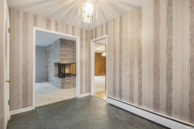 empty room with an inviting chandelier, a stone fireplace, and a baseboard radiator