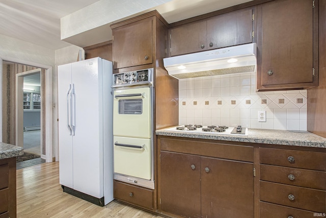 kitchen with dark brown cabinetry, light wood-type flooring, a baseboard heating unit, white appliances, and backsplash