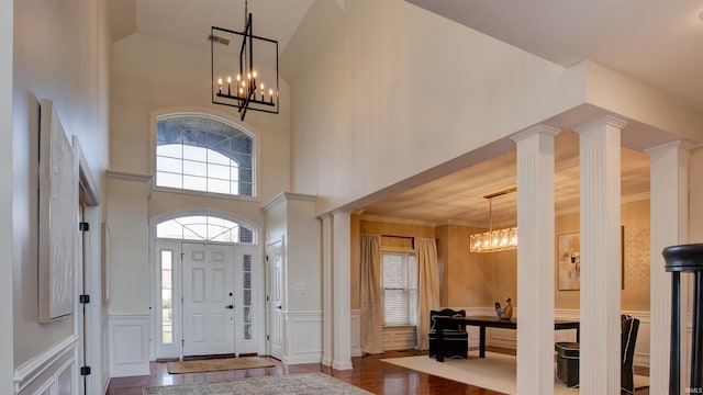 foyer with an inviting chandelier, a towering ceiling, dark hardwood / wood-style floors, and ornate columns