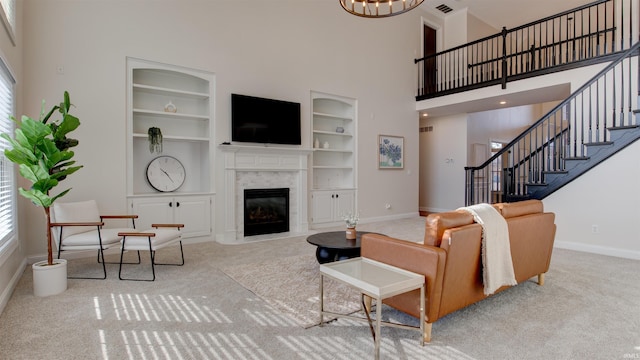 carpeted living room with built in shelves, a towering ceiling, plenty of natural light, and a premium fireplace