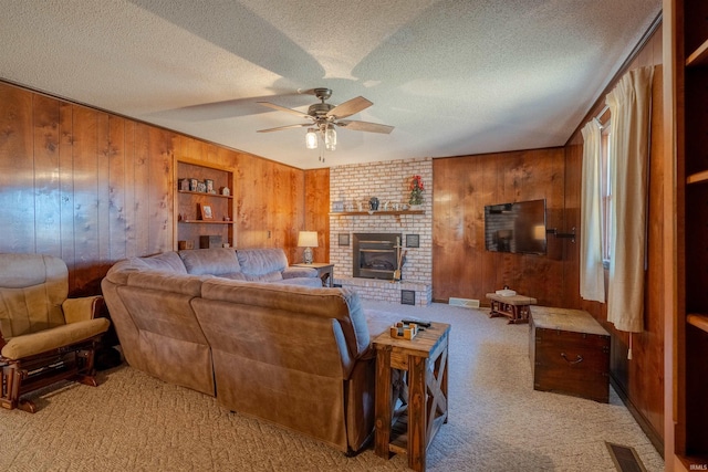 carpeted living room with a brick fireplace, wooden walls, a textured ceiling, and ceiling fan