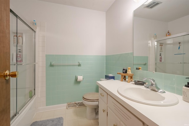 full bathroom featuring combined bath / shower with glass door, tile walls, vanity, tile patterned floors, and toilet