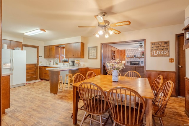 dining area with light hardwood / wood-style floors, ceiling fan, and wood walls