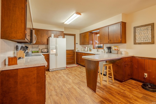 kitchen with backsplash, a kitchen breakfast bar, white fridge with ice dispenser, light hardwood / wood-style floors, and kitchen peninsula