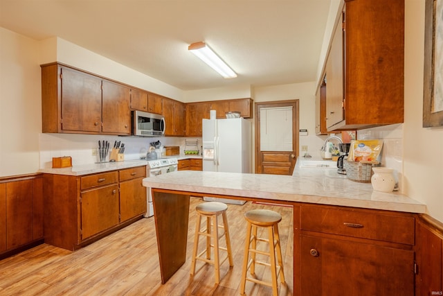 kitchen with sink, a kitchen breakfast bar, kitchen peninsula, white appliances, and light hardwood / wood-style floors