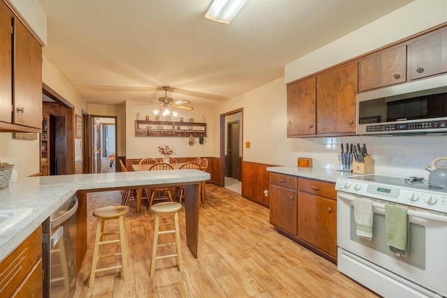 kitchen featuring a kitchen bar, decorative backsplash, ceiling fan, light hardwood / wood-style floors, and stainless steel appliances