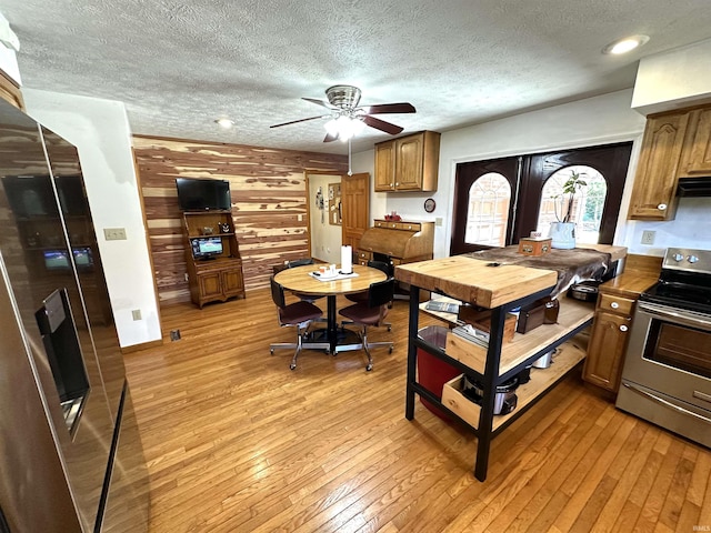 kitchen featuring wood walls, a textured ceiling, light wood-type flooring, electric range, and ceiling fan