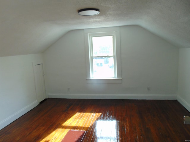 additional living space with dark hardwood / wood-style flooring, vaulted ceiling, and a textured ceiling