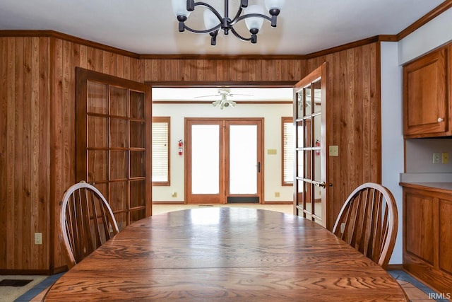 unfurnished dining area featuring french doors, ornamental molding, a notable chandelier, and wood walls