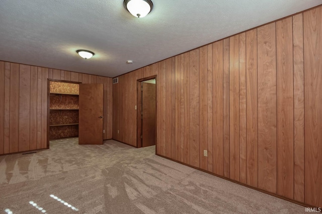 empty room featuring a textured ceiling, light carpet, and wood walls