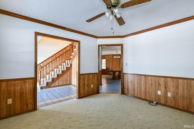 carpeted spare room with ceiling fan with notable chandelier, ornamental molding, a textured ceiling, and wood walls