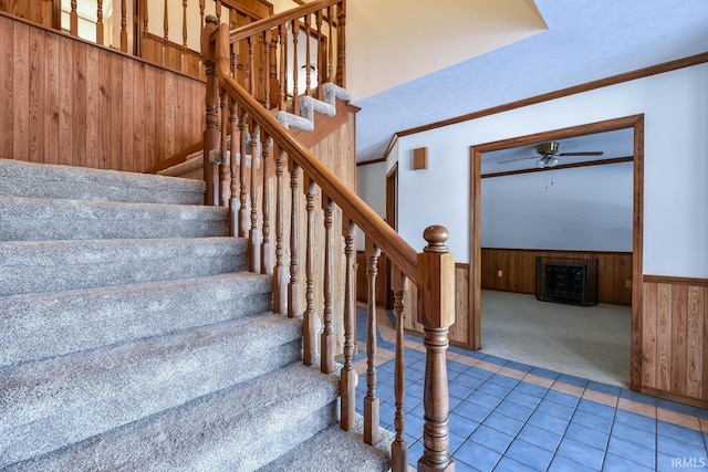 staircase with crown molding, carpet flooring, wooden walls, and ceiling fan