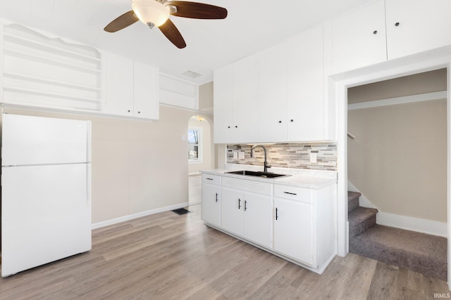 kitchen featuring sink, white cabinetry, light wood-type flooring, white refrigerator, and backsplash