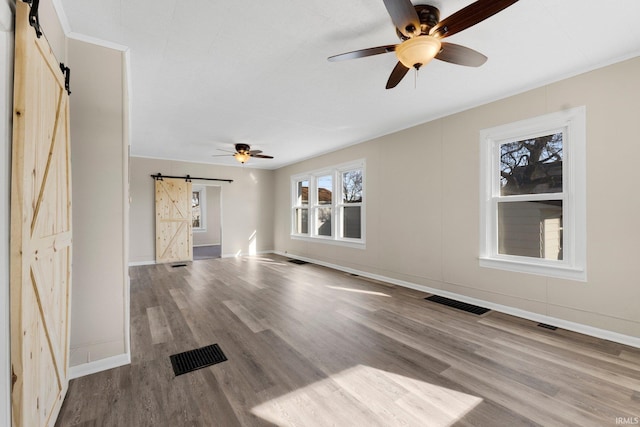 unfurnished living room featuring wood-type flooring, a barn door, and ceiling fan