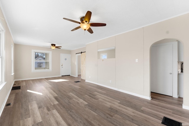 unfurnished living room featuring hardwood / wood-style flooring, ceiling fan, ornamental molding, and a barn door