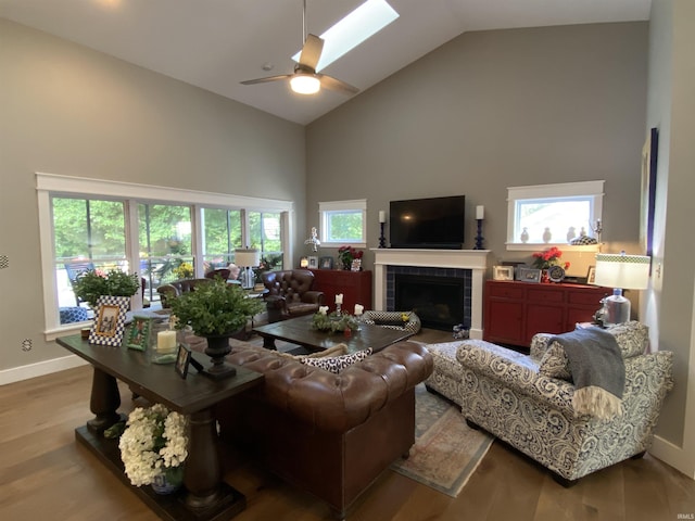 living room with a tile fireplace, high vaulted ceiling, a skylight, ceiling fan, and light wood-type flooring