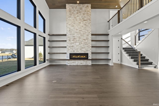 unfurnished living room with a fireplace, a towering ceiling, and dark wood-type flooring