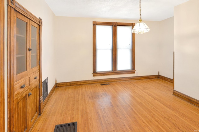 empty room featuring a notable chandelier and light hardwood / wood-style flooring