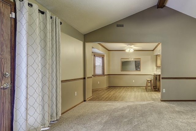 carpeted spare room featuring crown molding, lofted ceiling with beams, ceiling fan, and a textured ceiling