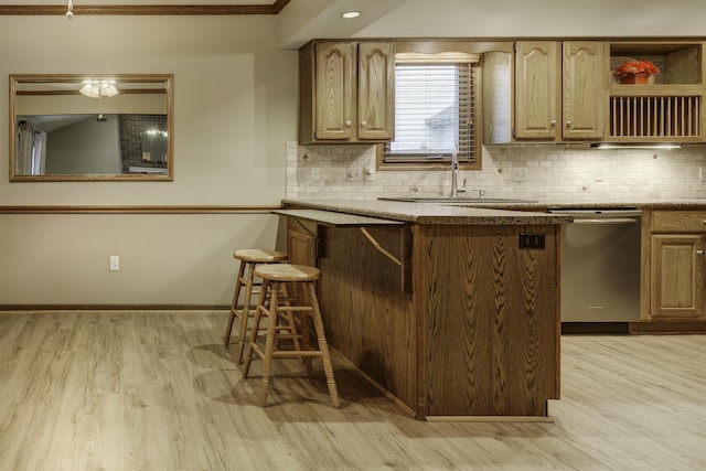 kitchen with sink, tasteful backsplash, stainless steel dishwasher, a kitchen breakfast bar, and light hardwood / wood-style floors