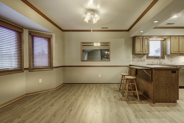 kitchen featuring a breakfast bar, tasteful backsplash, ornamental molding, light hardwood / wood-style floors, and kitchen peninsula