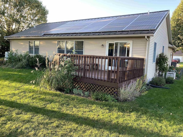 rear view of house featuring a wooden deck, a lawn, and solar panels