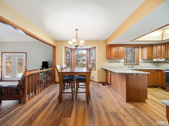 dining space with sink, a notable chandelier, light hardwood / wood-style flooring, and a textured ceiling