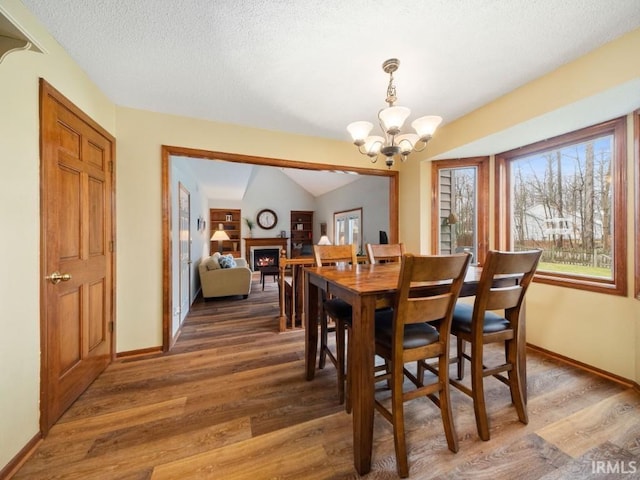 dining area with dark hardwood / wood-style flooring, a notable chandelier, vaulted ceiling, and a textured ceiling