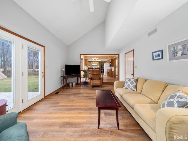 living room featuring high vaulted ceiling, a healthy amount of sunlight, a notable chandelier, and light wood-type flooring