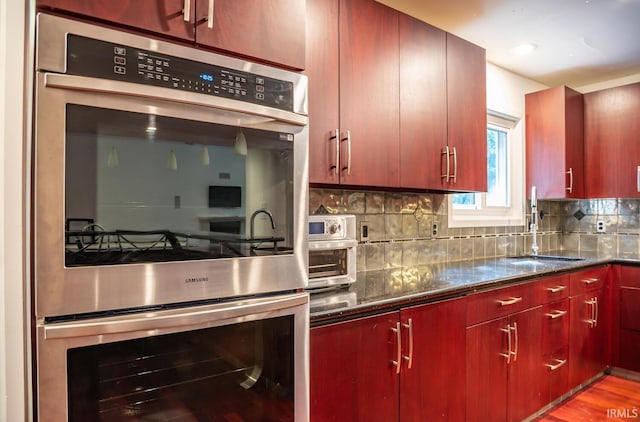 kitchen featuring sink, light hardwood / wood-style flooring, dark stone countertops, double oven, and tasteful backsplash