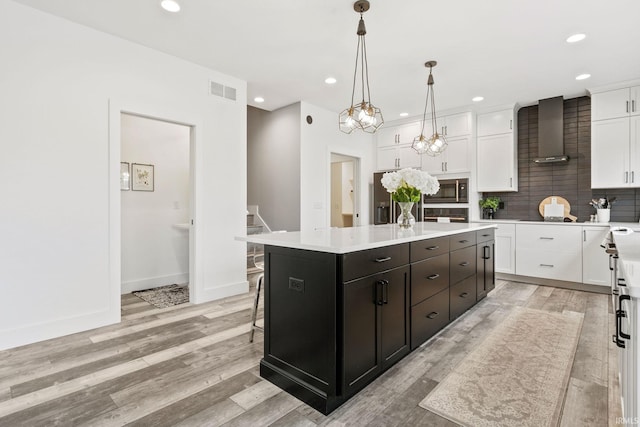 kitchen featuring pendant lighting, white cabinets, a kitchen island, built in microwave, and wall chimney exhaust hood