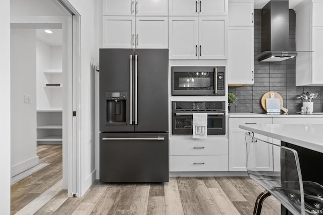 kitchen with light hardwood / wood-style flooring, wall chimney range hood, white cabinets, and black appliances