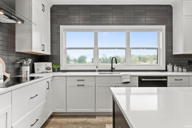 kitchen with a wealth of natural light, tasteful backsplash, white cabinetry, black electric stovetop, and wall chimney range hood