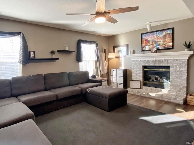 living room featuring a brick fireplace, wood-type flooring, and ceiling fan