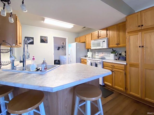 kitchen featuring sink, a breakfast bar area, white appliances, washer / clothes dryer, and hardwood / wood-style floors