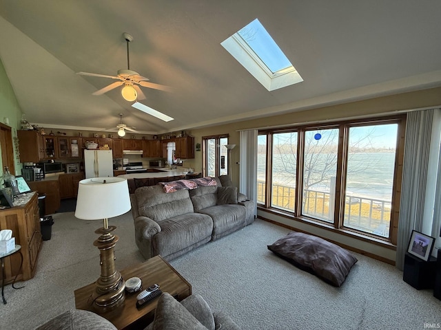 carpeted living room with a water view, ceiling fan, plenty of natural light, and lofted ceiling with skylight